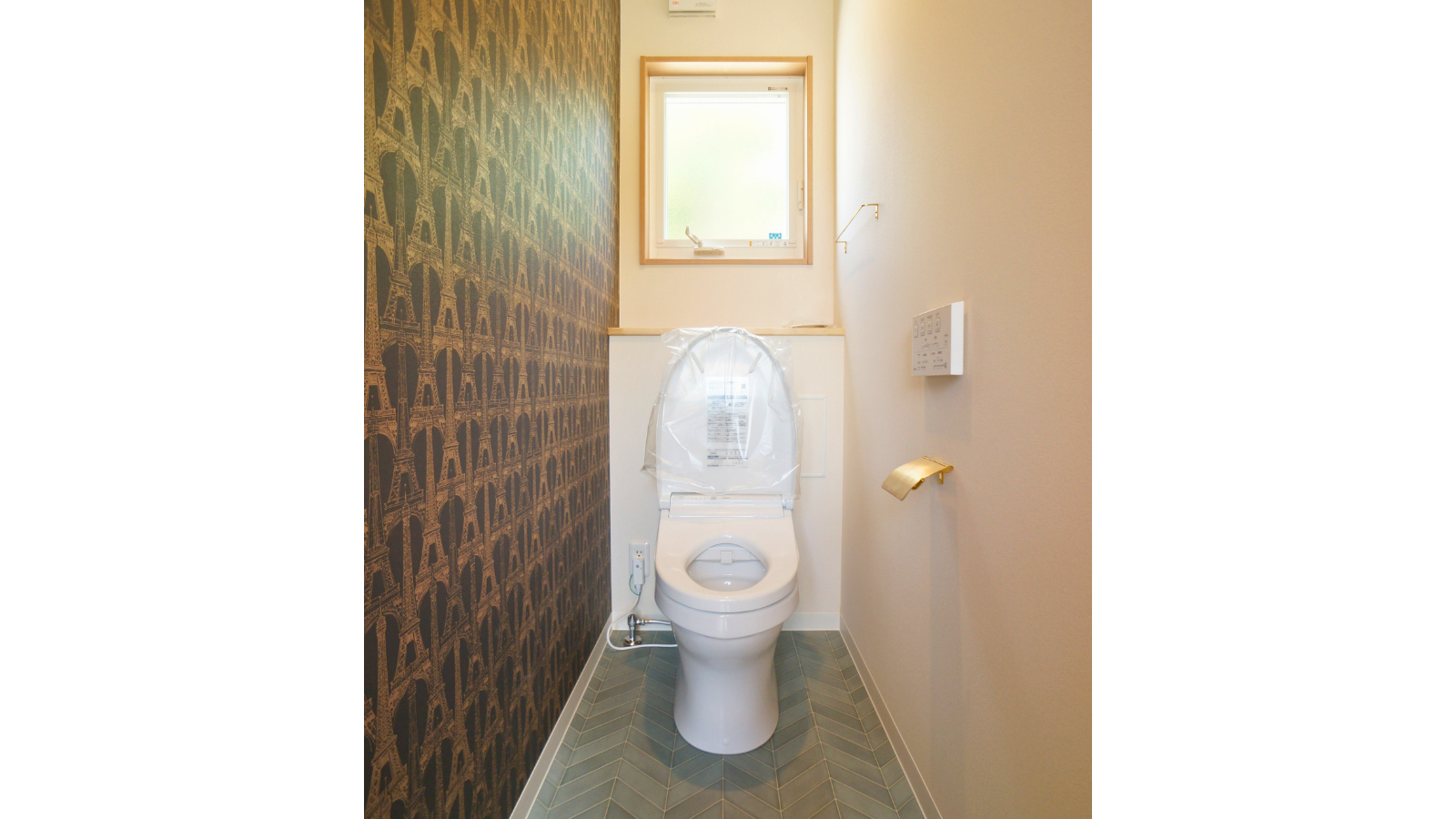 クラシックな柄のアクセントクロスとヘリンボーン柄の床を組み合わせた、おしゃれなトイレ空間。真鍮のペーパーホルダーがアクセント